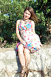 Emily 18 sits on a rock outdoors on touching the brush cute flowered dress and she smiles at one\