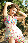 Emily 18 sits on a rock outdoors on touching the brush cute flowered dress and she smiles at one\